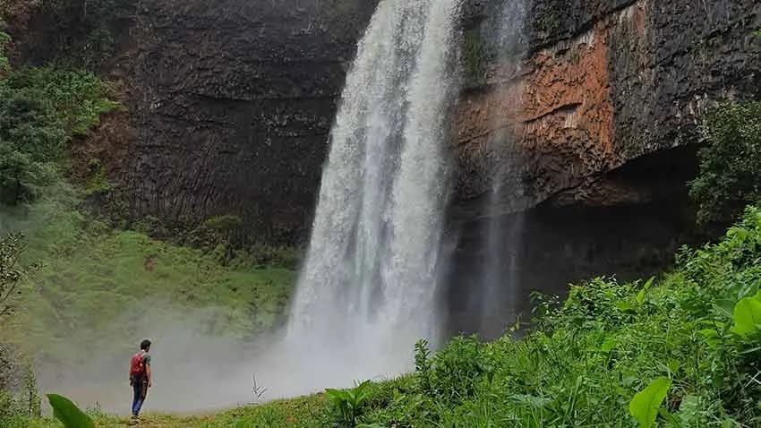Cachoeira em área de mata preservada, com pessoa ao pé da queda dando escala