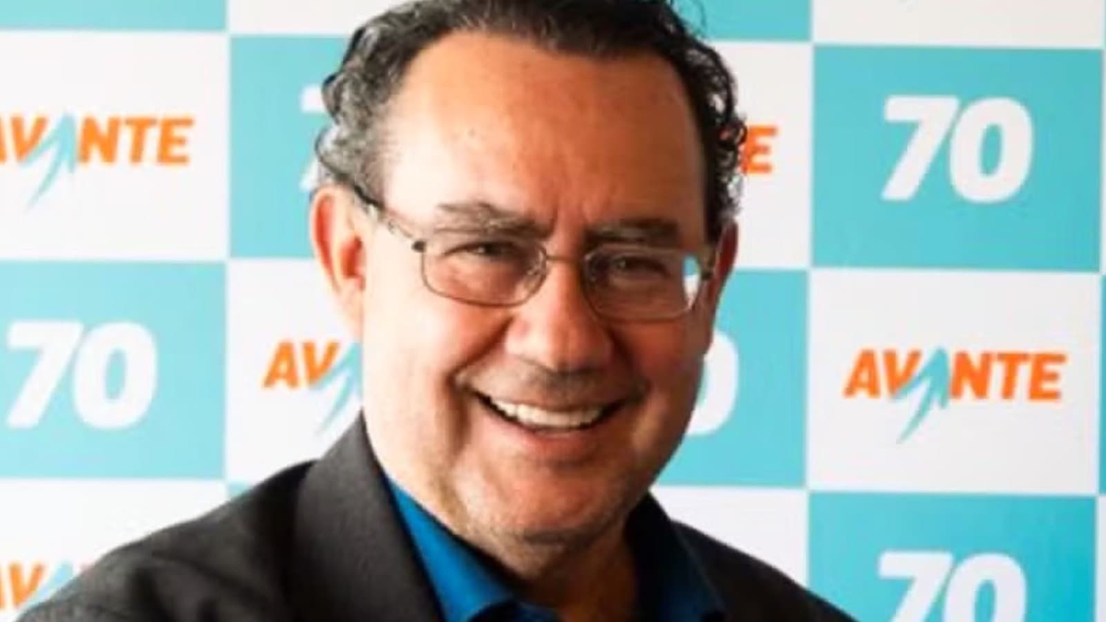 Retrato de Augusto Cury sorrindo, com óculos, em frente a painel do partido Avante com o número 70