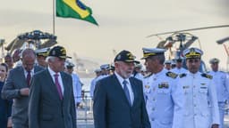 Lula caminha ao lado de autoridades e oficiais da Marinha do Brasil em navio, com bandeira nacional ao fundo (foto de arquivo)