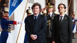 Javier Milei em cerimônia oficial, usando terno escuro, cercado por guarda de honra