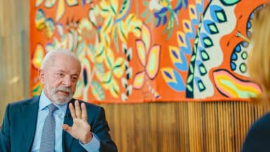 Lula gesticula durante entrevista de televisão, com painel colorido ao fundo