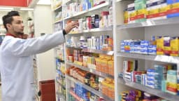 Farmacêutico organiza medicamentos em prateleira de farmácia