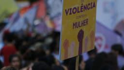 Cartaz com os dizeres 'fim da violência contra a mulher' erguido em meio a manifestação, com punhos cerrados ilustrados