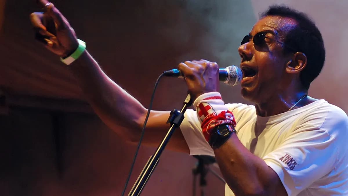 Jorge Ben Jor canta no microfone durante show, com o braço levantado