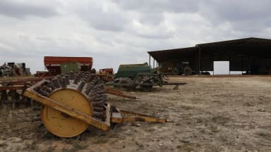 Maquinário agrícola parado em fazenda, com galpão ao fundo, imagem de arquivo