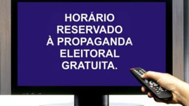 Televisão exibindo tela roxa com o aviso "Horário reservado à propaganda eleitoral gratuita" e mão segurando controle remoto
