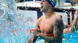 Nadador brasileiro comemora dentro da piscina, com touca do Brasil, em meio a respingos de água