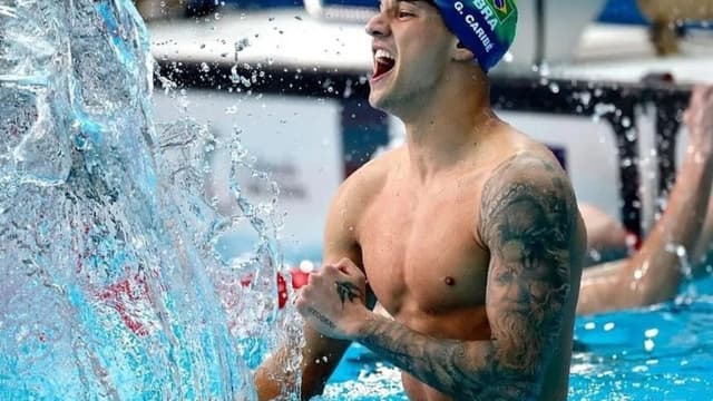 Nadador brasileiro comemora dentro da piscina, com touca do Brasil, em meio a respingos de água