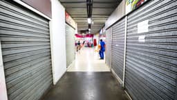 Corredor de galeria comercial com lojas fechadas por portas metálicas