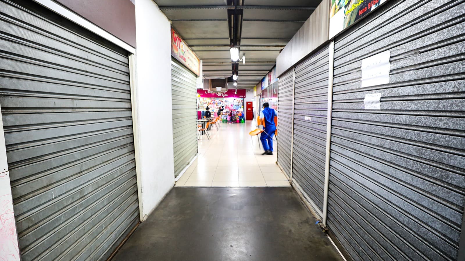 Corredor de galeria comercial com lojas fechadas por portas metálicas