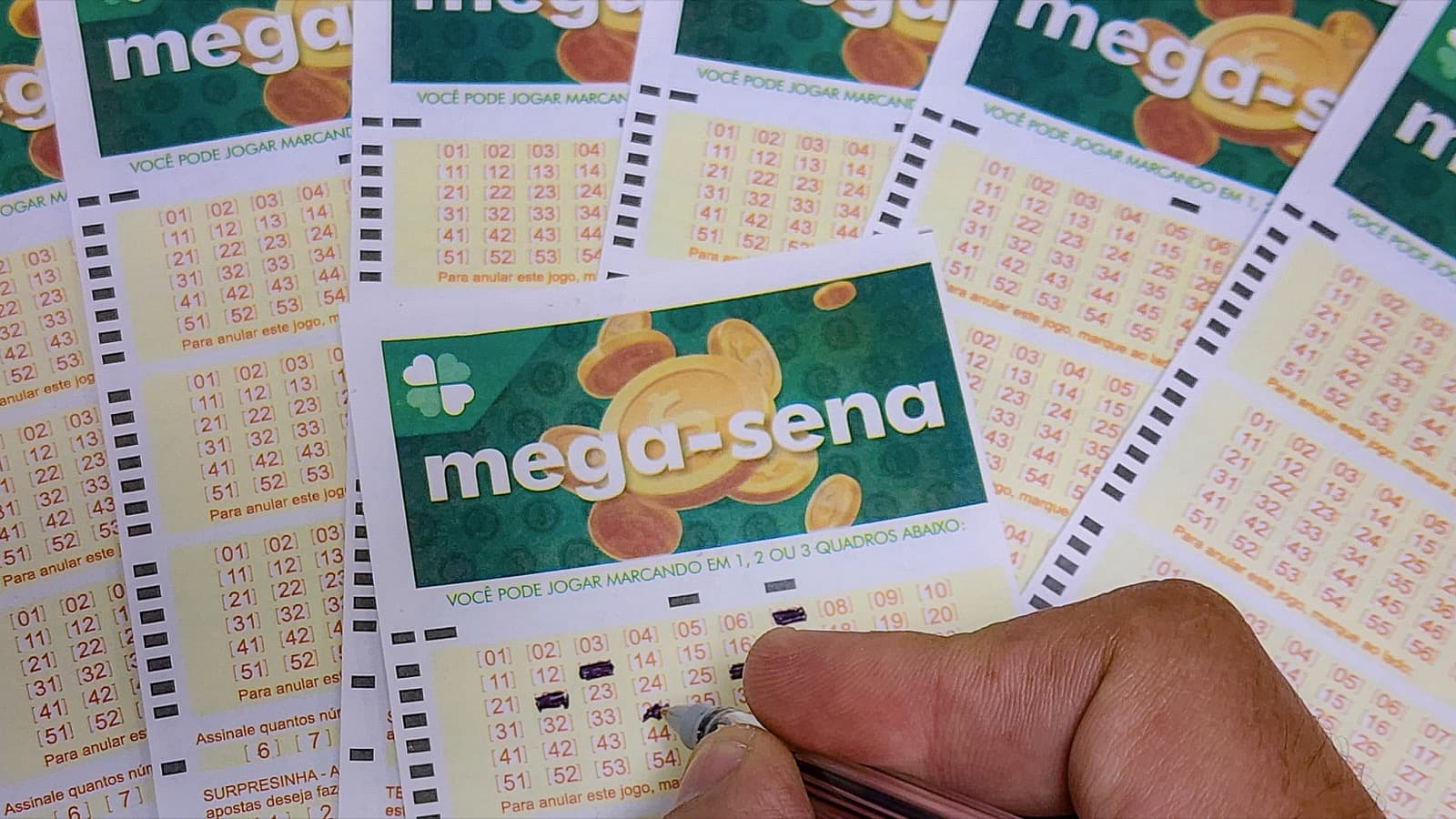 Mão preenche volante de aposta da Mega-Sena sobre outros volantes em casa lotérica