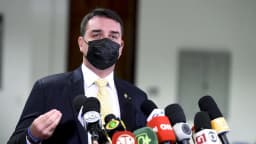 Flávio Bolsonaro fala à imprensa em coletiva, cercado por microfones de emissoras
