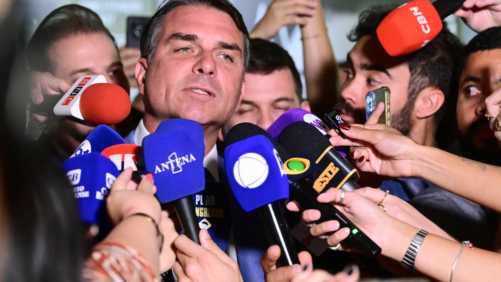 Flávio Bolsonaro rodeado por microfones de emissoras de TV durante entrevista coletiva no Senado
