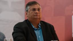 Ministro Flávio Dino observa atentamente durante evento, vestindo terno escuro
