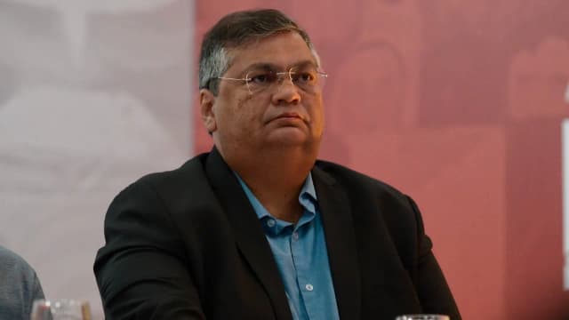 Ministro Flávio Dino observa atentamente durante evento, vestindo terno escuro