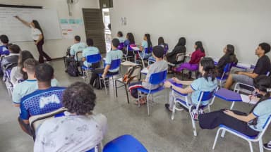 Professora dá aula de matemática num quadro branco para turma de estudantes do ensino médio