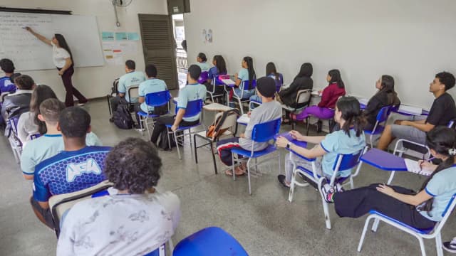 Professora dá aula de matemática num quadro branco para turma de estudantes do ensino médio