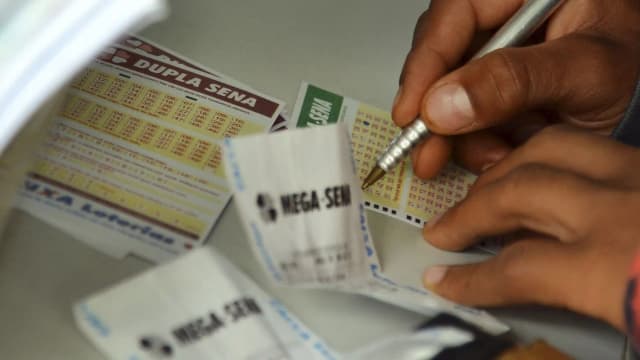 Mãos preenchendo um cartão de aposta da Mega-Sena