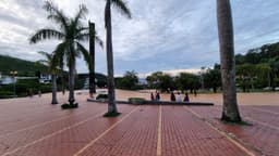 Vista da Praça do Papa, em Belo Horizonte, com o piso vermelho, palmeiras e pessoas sentadas em um banco ao fundo. Imagem de arquivo de fevereiro de 2023, antes da reforma.