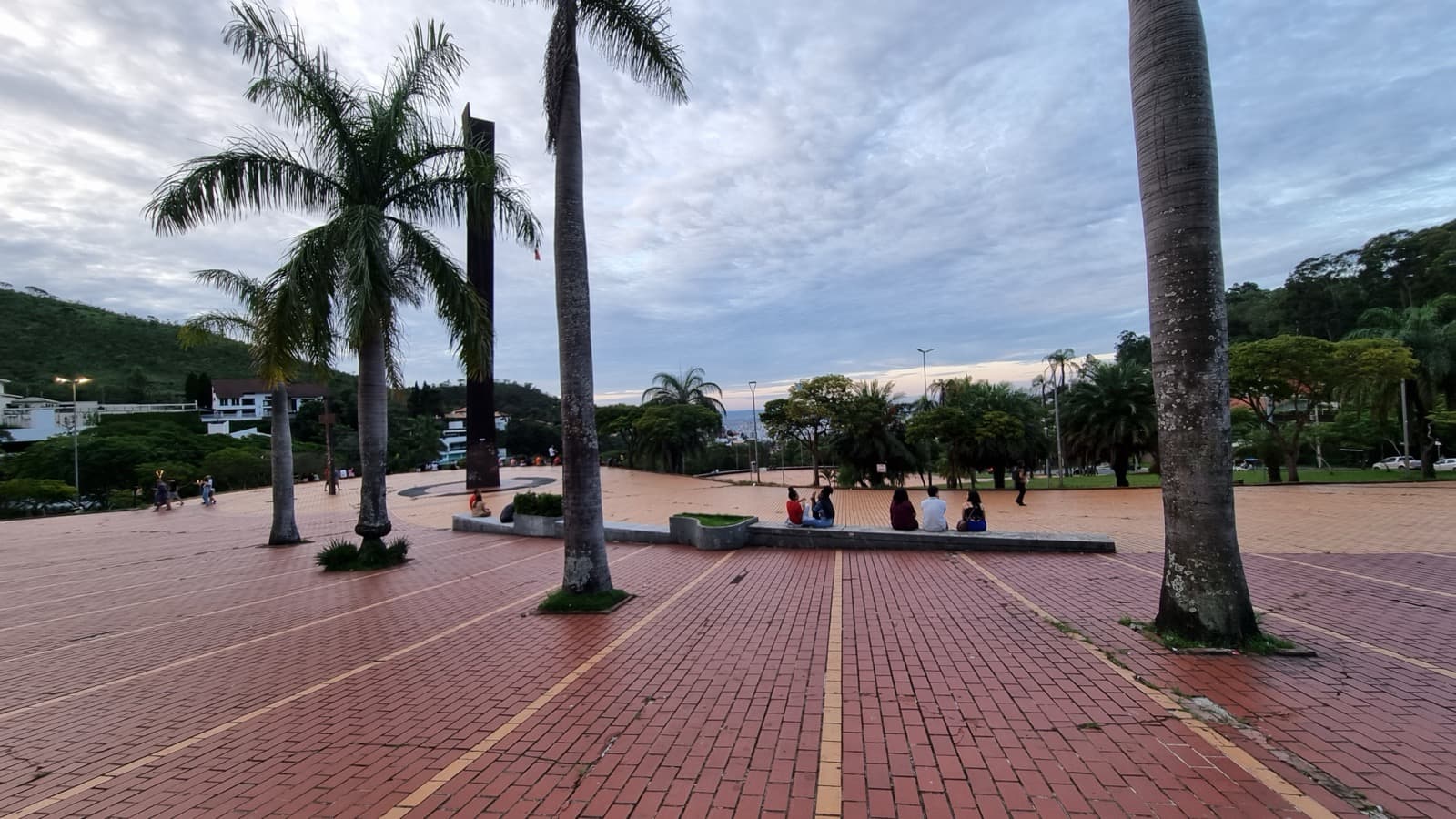 Vista da Praça do Papa, em Belo Horizonte, com o piso vermelho, palmeiras e pessoas sentadas em um banco ao fundo. Imagem de arquivo de fevereiro de 2023, antes da reforma.