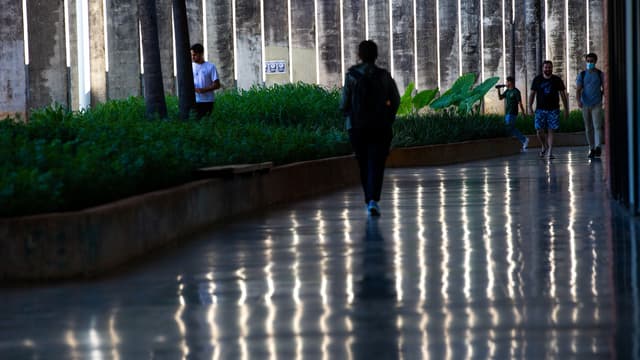 Estudantes caminham por um corredor coberto de campus universitário, com jardim ao lado e piso refletindo a luz. Foto de arquivo, sem relação direta com a chamada UniCuidotecas.