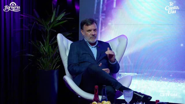 Alessandro Feijó fala com o dedo indicador erguido durante entrevista ao programa Te Conto, Uai, em estúdio com luzes roxas
