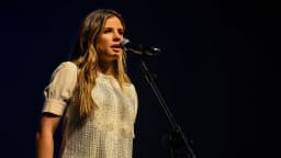 Giulia Be cantando ao microfone em show, com vestido branco