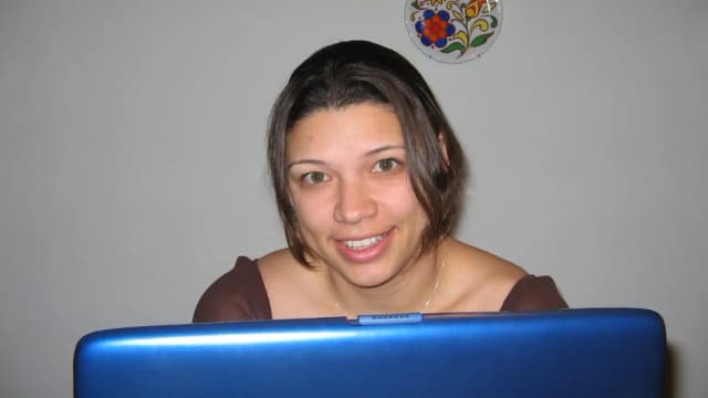 Mulher sorrindo atrás da tela de um notebook aberto