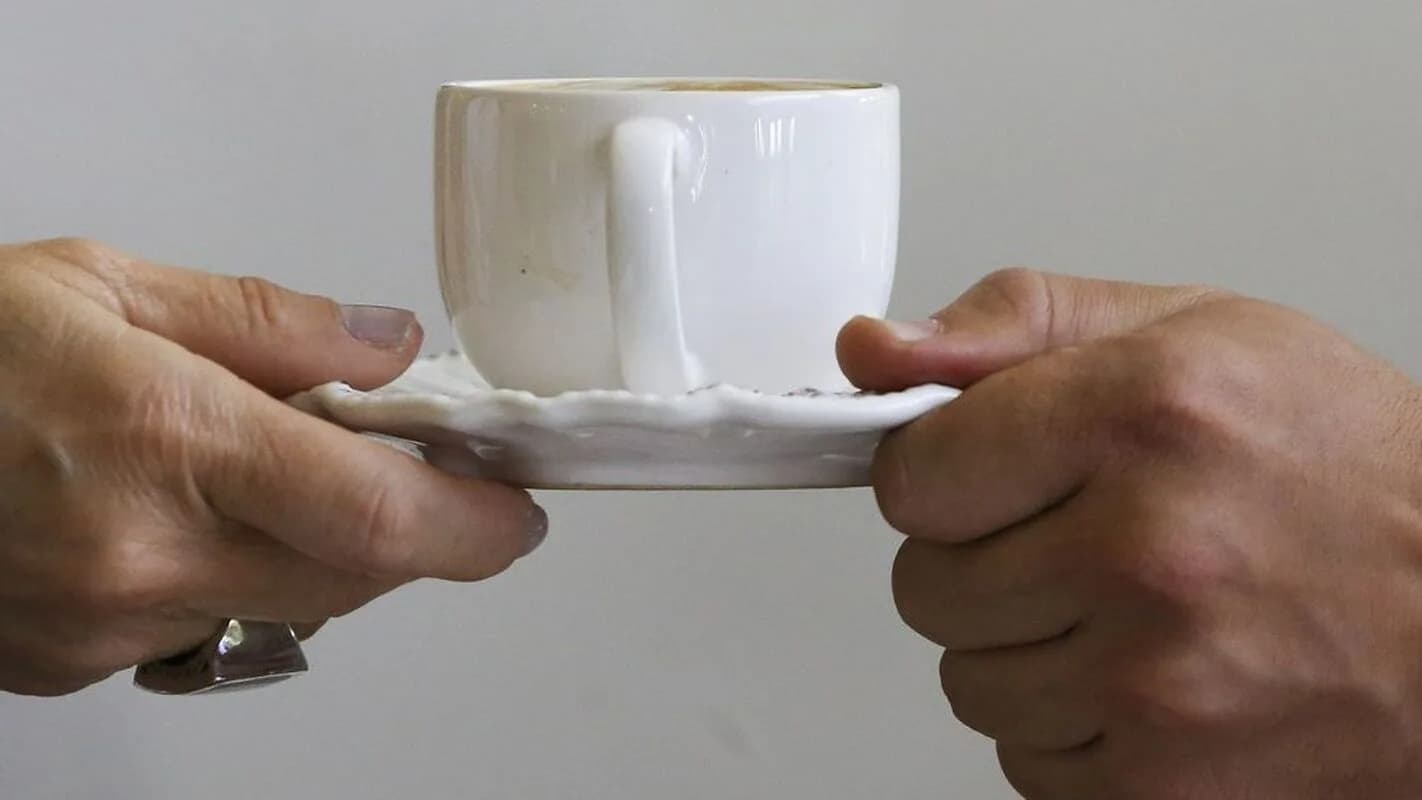 Duas mãos servem uma xícara de café especial em pires branco