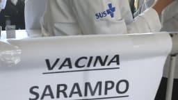 Faixa 'Vacina Sarampo' em posto de vacinação com agente de saúde do SUS ao fundo