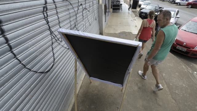 Cavalete de propaganda eleitoral em calçada, com pessoas passando ao fundo