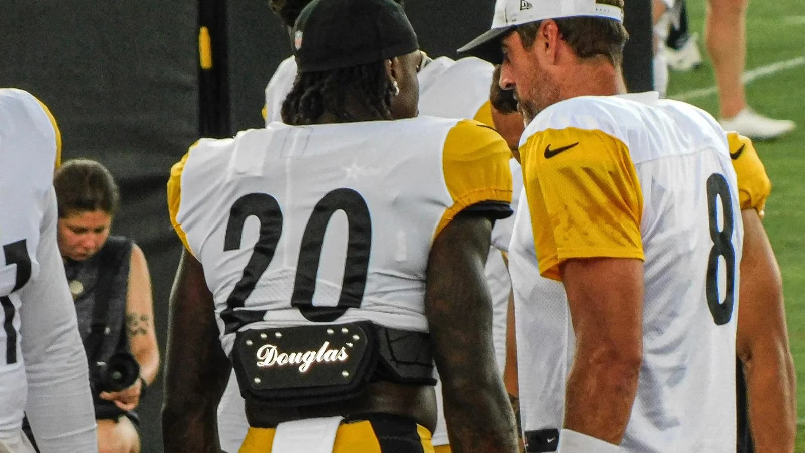 Aaron Rodgers, com boné branco, conversa com um companheiro de equipe durante treino dos Pittsburgh Steelers