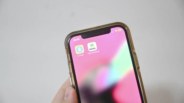 Mão segura celular com o aplicativo e-Título aberto, símbolo das Eleições 2026