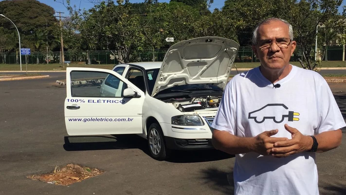 Homem ao lado de carro convertido para elétrico, com capô aberto mostrando o motor