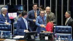 Senadores cumprimentam-se sorridentes no plenário do Senado Federal durante sessão solene