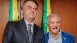 Carlos Alberto de Nóbrega sorri ao lado de outro homem de terno, em evento oficial