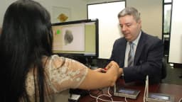 Eleitora tem digital coletada em cadastro biométrico eleitoral, com técnico auxiliando no equipamento