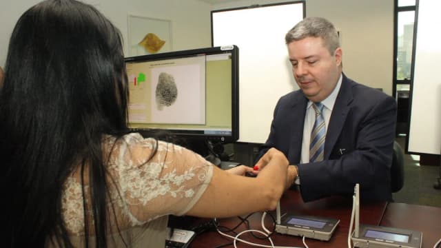 Eleitora tem digital coletada em cadastro biométrico eleitoral, com técnico auxiliando no equipamento