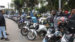 Motociclistas de aplicativo reunidos em via pública, ao lado de motos com baús de entrega, em foto de arquivo