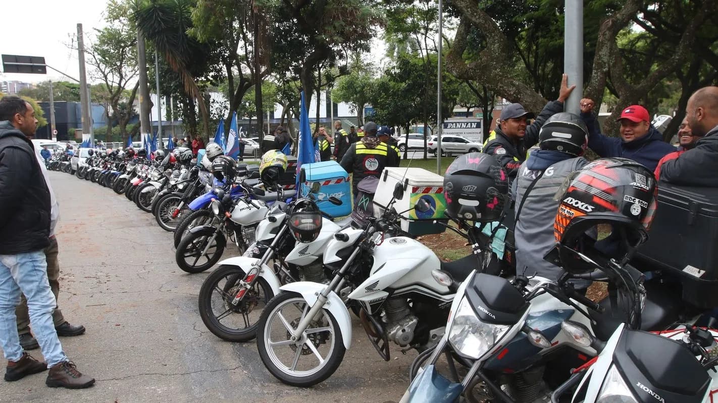 Motociclistas de aplicativo reunidos em via pública, ao lado de motos com baús de entrega, em foto de arquivo