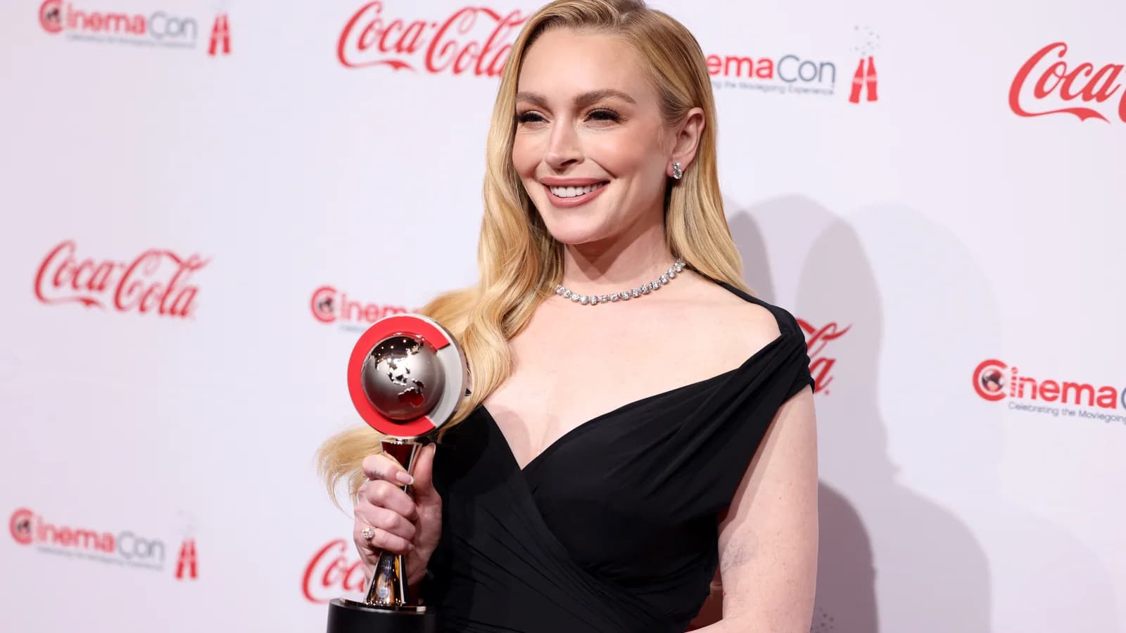 Lindsay Lohan sorri em tapete vermelho, usando vestido preto, em evento recente