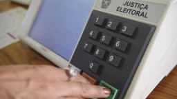 Mão de eleitor digitando número na urna eletrônica da Justiça Eleitoral