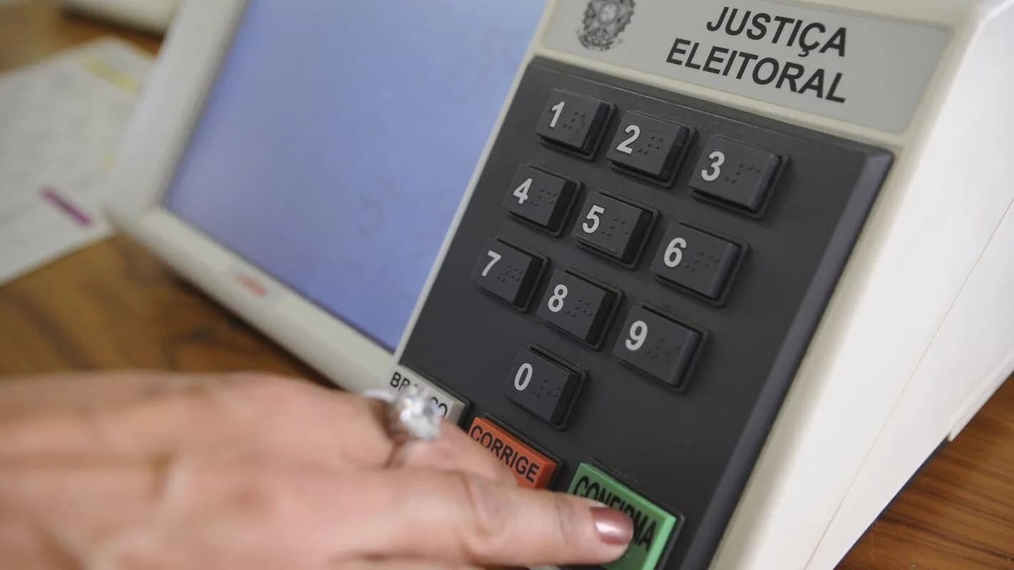 Mão de eleitor digitando número na urna eletrônica da Justiça Eleitoral