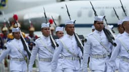 Militares brasileiros em uniforme de gala desfilam com fuzis, ao fundo aeronave da Força Aérea Brasileira