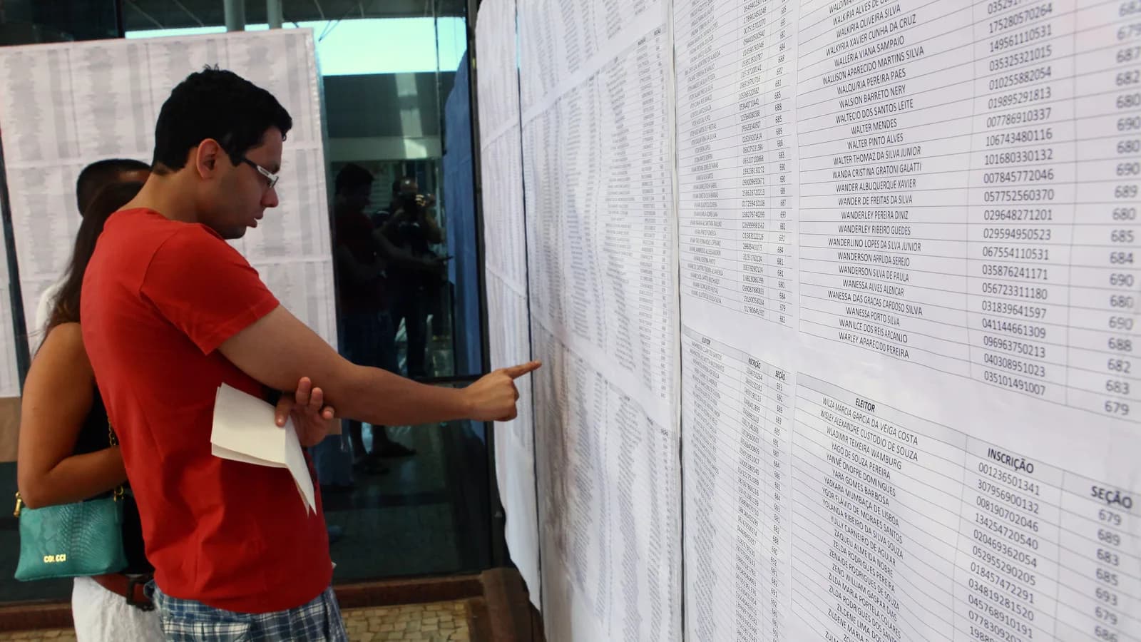 Eleitores conferem lista de candidatos em painel afixado em seção eleitoral