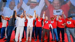 Lula em ato de campanha, com braços erguidos ao lado de aliados