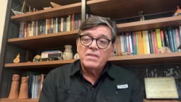 O cientista político Manoel Santos, de óculos e camisa preta, fala em entrevista por videochamada com estante de livros ao fundo