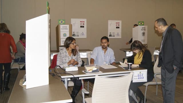 Brasileiros votam em seção eleitoral de consulado no exterior, com cabines e urnas identificadas com a bandeira do Brasil