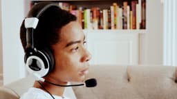 Jovem com fone de ouvido e microfone jogando videogame em frente a uma tela