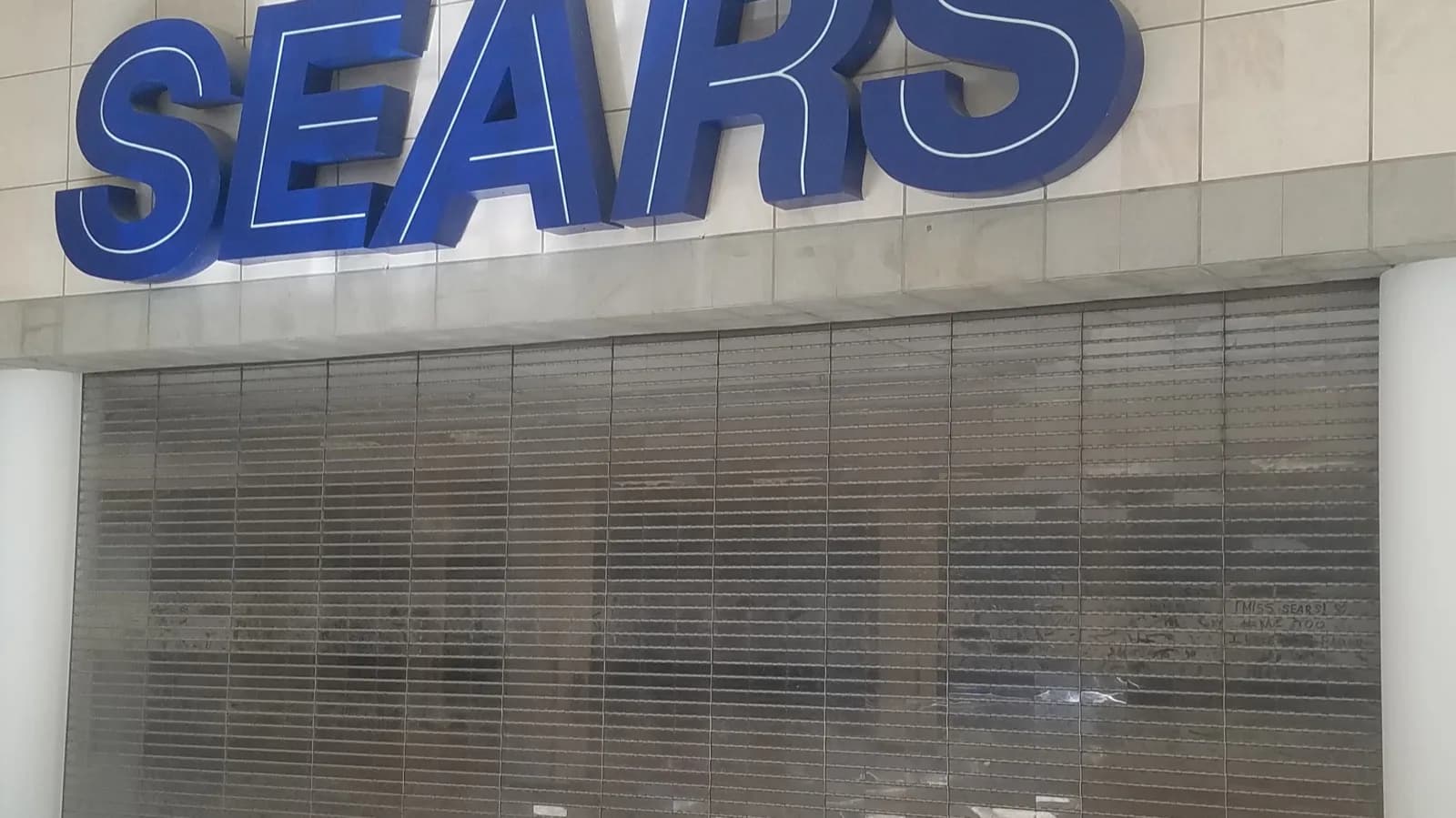Fachada de loja fechada com porta de aço puxada em shopping, com placa de loja fechada